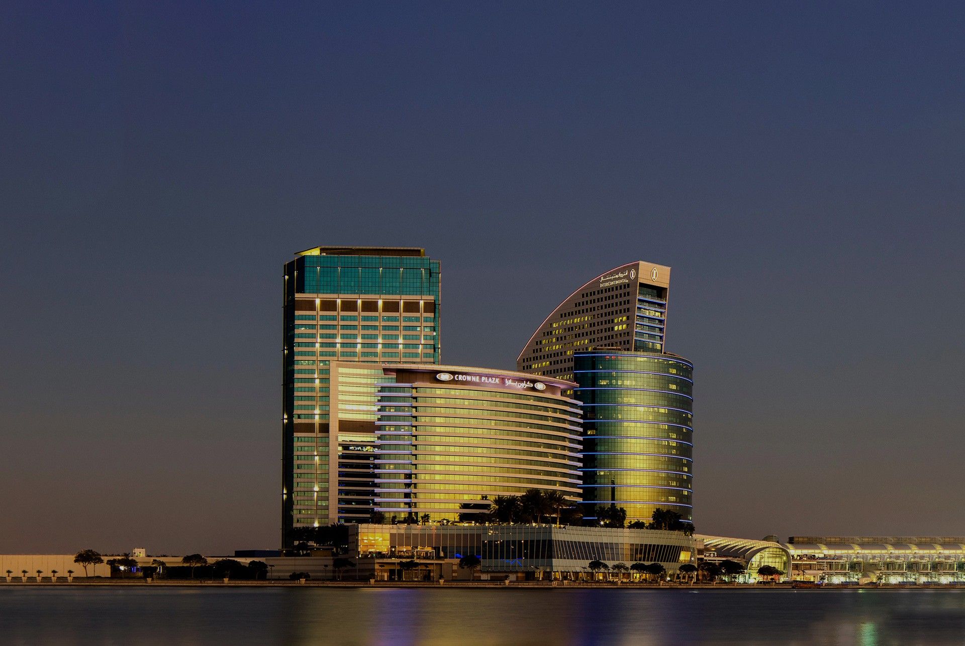 The InterContinental and Crowne Plaza towers at Dubai Festival City lit at dusk, seen across the creek